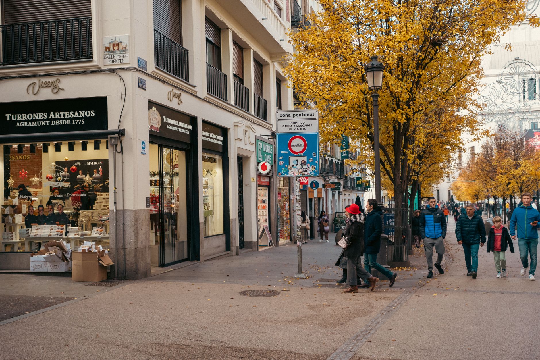 Pedestrians enjoy a stroll in Madrid's autumn street with vibrant yellow trees and shops.